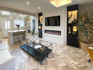 A modern living room with a glass coffee table, a fireplace, a TV mounted on the wall, and a kitchen area visible through an open door. - 2 bedroom accommodation in Newcastle Upon Tyne (Newcastle Upon Tyne)