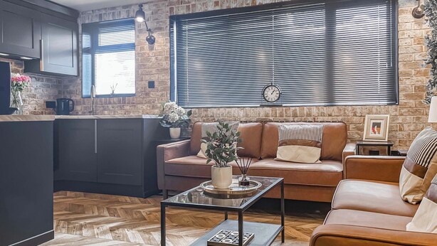 Une cuisine moderne avec des meubles de couleur sombre, une machine à café et un mur en briques.