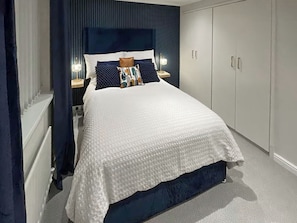 Une chambre à coucher avec un lit, des tables de chevet, une commode et une fenêtre avec des rideaux.
