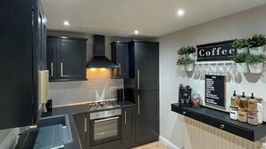 A modern kitchen with dark cabinetry, a built-in oven, a coffee station with dispensers, and a sign indicating coffee options. - 2 bedroom accommodation in Newcastle Upon Tyne (Newcastle Upon Tyne)