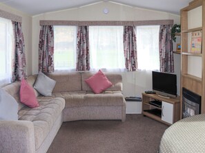 A living room with a beige sofa, pink cushions, a television on a wooden stand, and a bookshelf. - 2 bedroom accommodation in Llanbedr, near Harlech (Llanbedr, near Harlech)