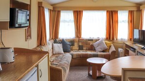 Ein kompakter Wohnraum mit einer Küchenzeile, einem Sofa, einem Esstisch und einem Fernseher.
