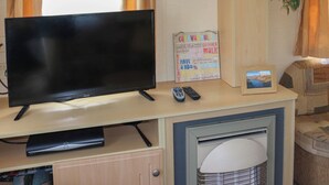 Ein Fernseher auf einem Holztisch mit Fernbedienung, einem gerahmten Bild und einem Schild mit Text.