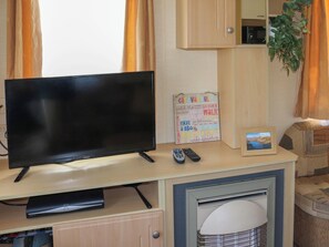 A TV on a wooden desk with a remote, a framed picture, and a sign with text. - 2 bedroom accommodation in Llanbedr, near Harlech (Llanbedr, near Harlech)
