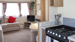 Ett kompakt bostadsutrymme med en soffa, TV, köksdel och ett matbord.