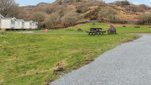 En campingplats med picknickbord, en grusgång och en rad husvagnar i bakgrunden.