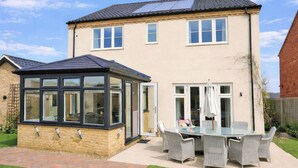 A two-story house with a conservatory, a patio with wicker furniture, and a brick pathway. - 4 bedroom accommodation in Holt (Holt)
