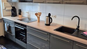 A modern kitchen with a built-in oven, a coffee maker, and a kettle on the countertop.