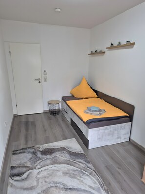 A bedroom with a bed, a small round side table, a white door, and a shelf with plants. - Apartment '4Zi Kü, Balkon Parknähne' with Balcony and Wi-Fi (Neunkirchen)