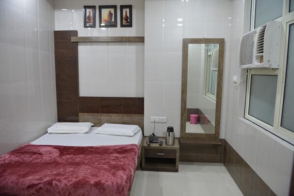Habitación de hotel con cama, mesita de noche, espejo y aire acondicionado.