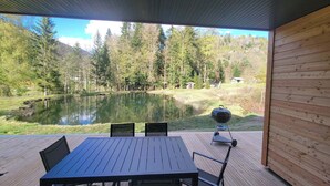 A covered outdoor deck with a table and chairs, overlooking a lake and forested hills. - Chalet des Briseux (Saint-Maurice-sur-Moselle)