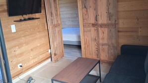A room with wooden walls, a flat-screen TV mounted on the wall, a sliding door, a sofa, and a small table. - Chalet des Briseux (Saint-Maurice-sur-Moselle)