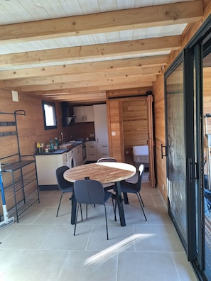 A wooden interior with a dining table, chairs, a kitchen area, and a sliding glass door.