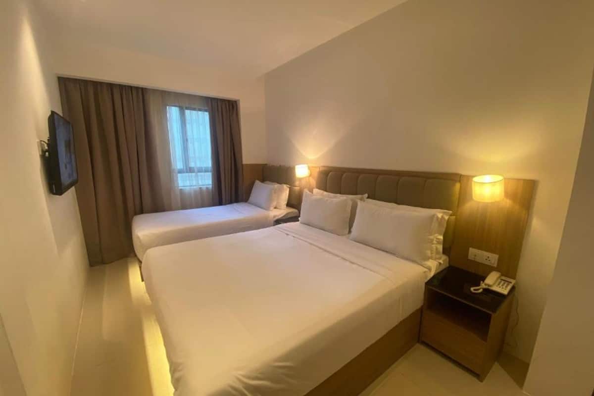 Une chambre d’hôtel avec deux lits, une table de chevet avec un téléphone et une fenêtre avec des rideaux.