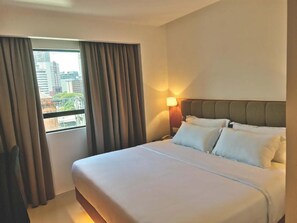 Une chambre d’hôtel avec un grand lit, une table de chevet, une lampe et une fenêtre avec des rideaux.