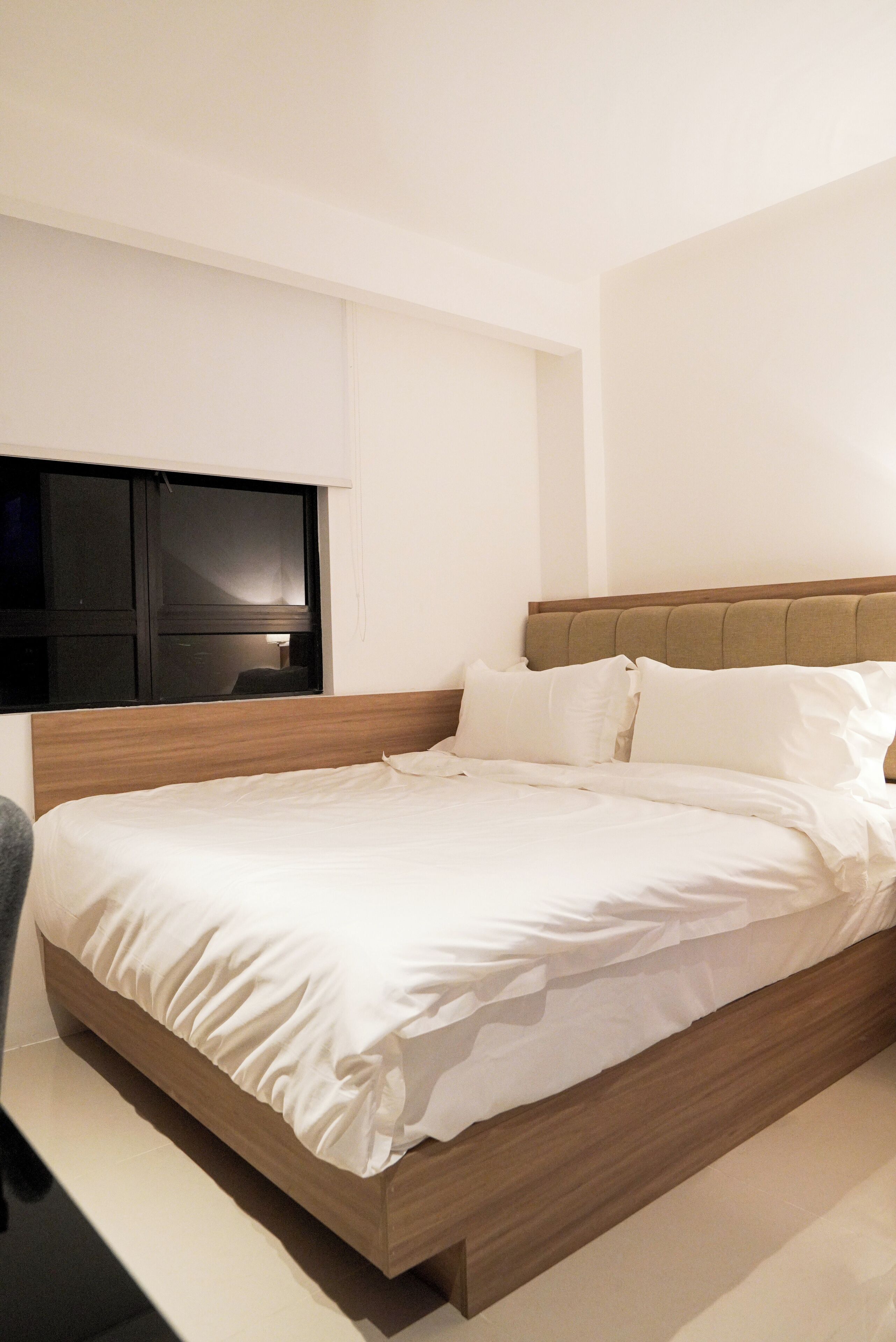 Une chambre à coucher moderne avec un cadre de lit en bois, une literie blanche et un téléviseur à écran plat fixé au mur.