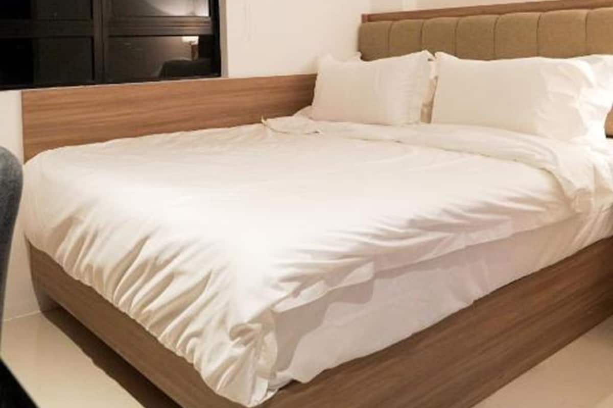 Une chambre à coucher moderne avec un cadre de lit en bois, une literie blanche et un téléviseur à écran plat fixé au mur.