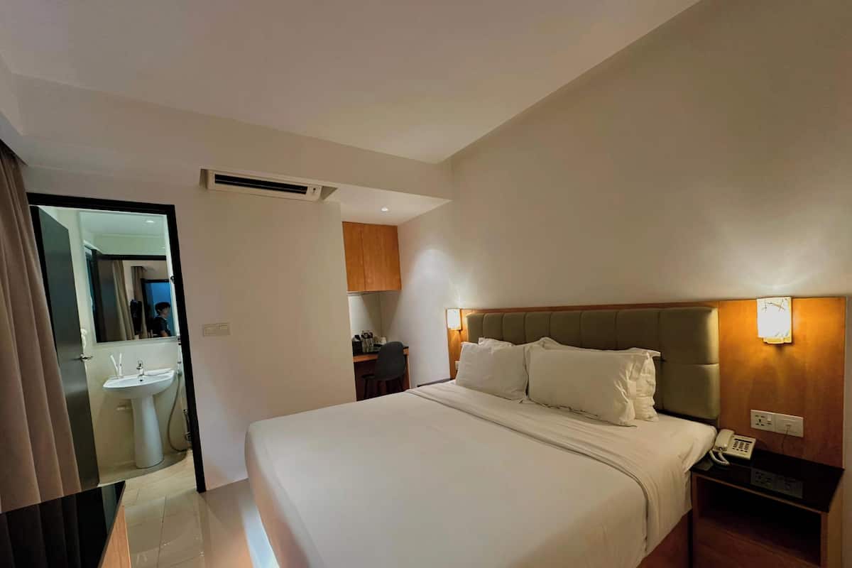 Une chambre d’hôtel avec un grand lit, une table de chevet avec un téléphone, un bureau avec une chaise et une salle de bain équipée d’un lavabo et d’un miroir.