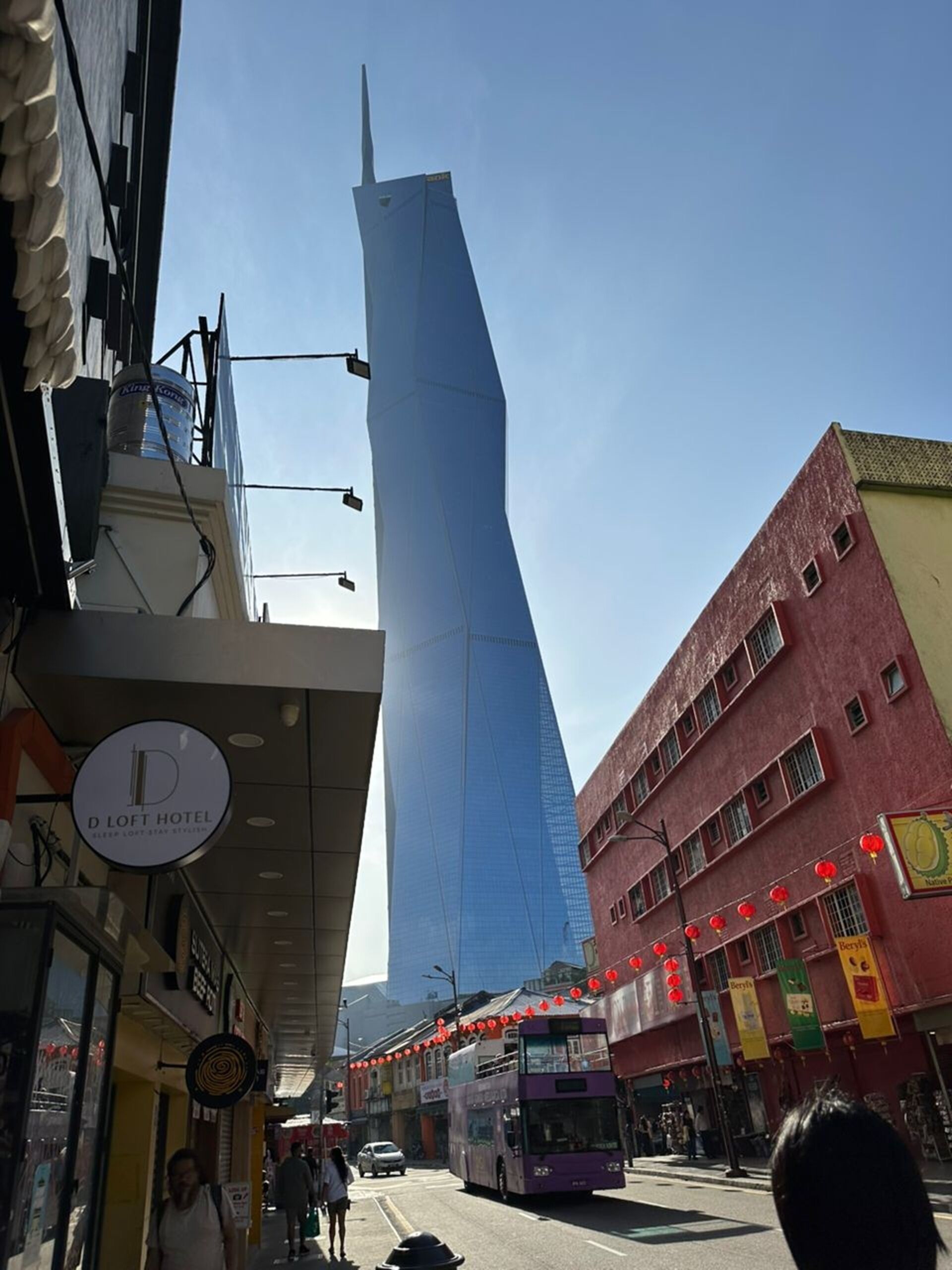 A modern building with a unique angular design, a D Loft Hotel sign, and a traditional building with red lanterns.