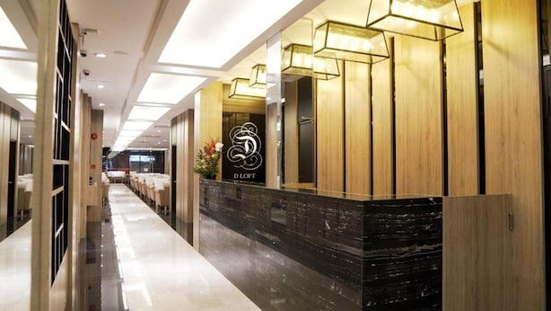 Uma área de recepção de hotel com design moderno, apresentando um balcão de atendimento, um logotipo e um corredor que dá para os quartos de hóspedes.