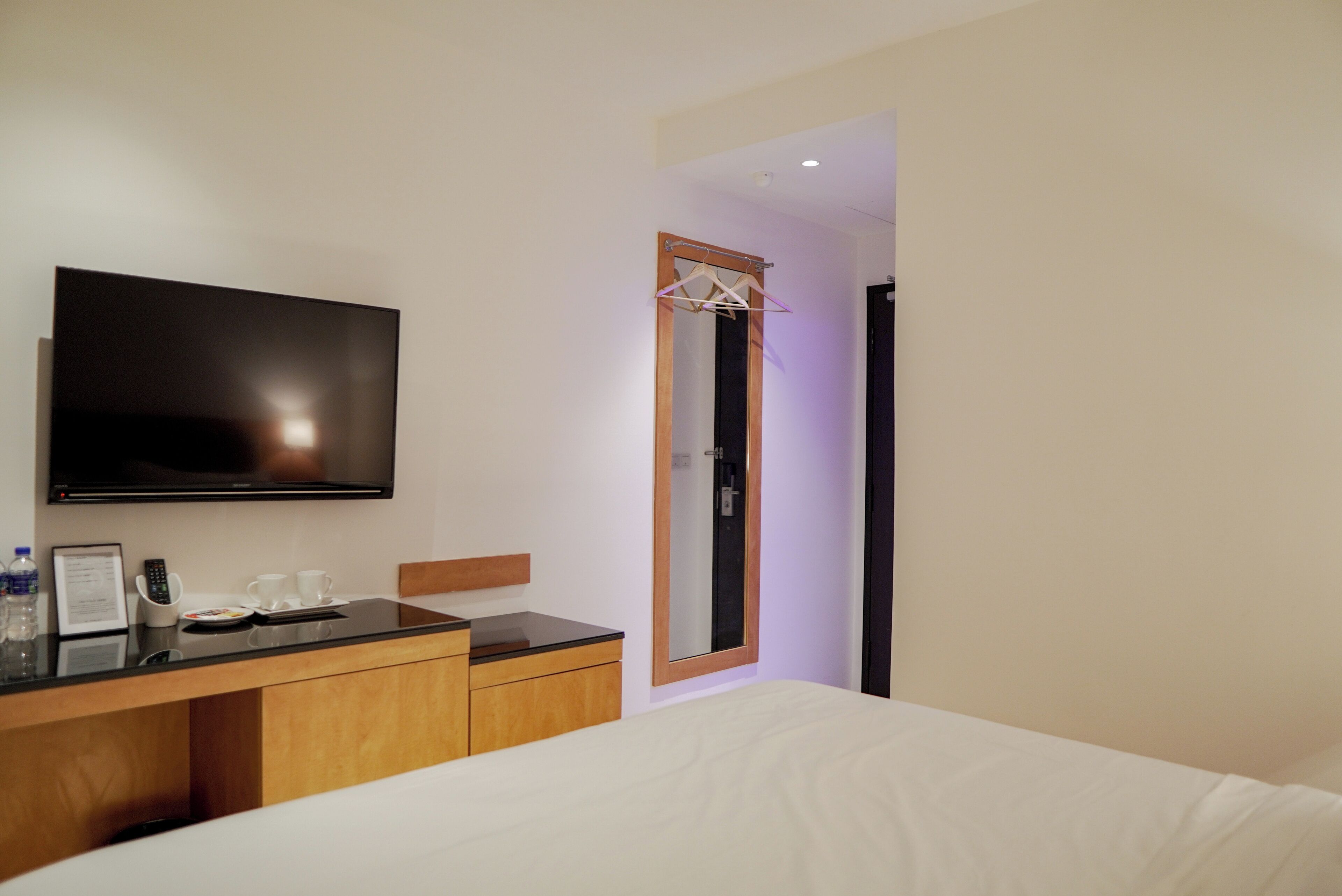 Une chambre d’hôtel avec un lit, un téléviseur fixé au mur, une commode en bois et un miroir.