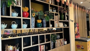 Paredes com prateleiras exibindo diversos objetos, incluindo bules, vasos e plantas decorativas.