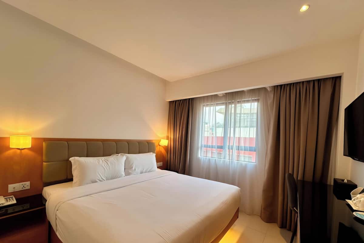Une chambre d’hôtel avec un lit, des lampes de chevet, une télévision et une fenêtre avec des rideaux.
