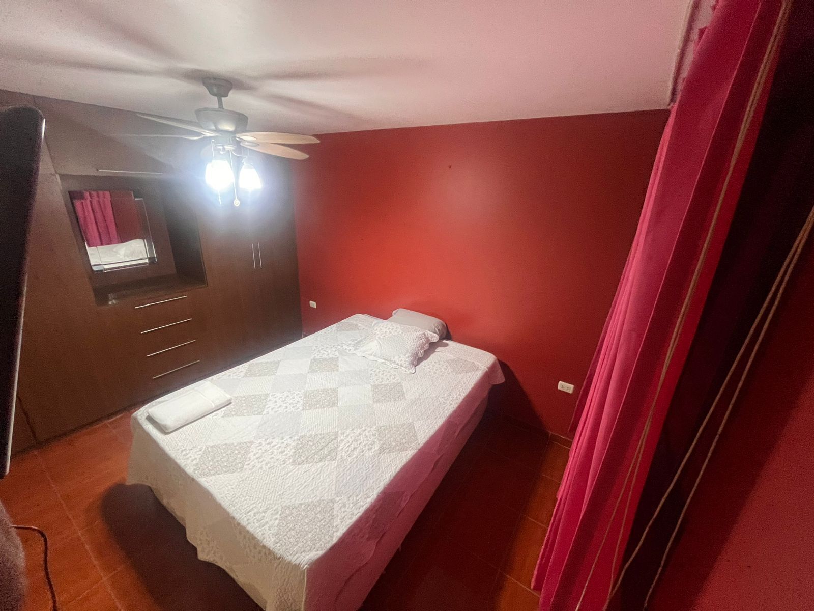 Un dormitorio con cama, armario, ventilador de techo y ventana con cortinas.