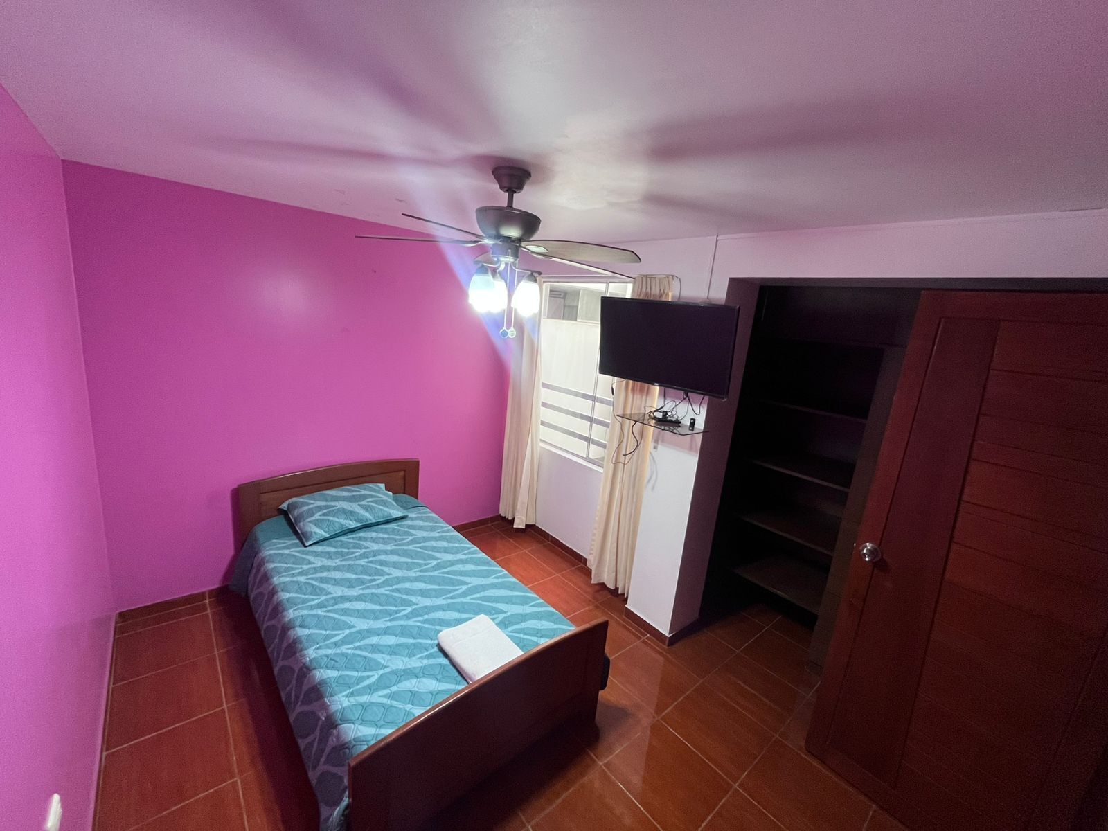A bedroom with a bed, a ceiling fan, a TV, and a wardrobe.