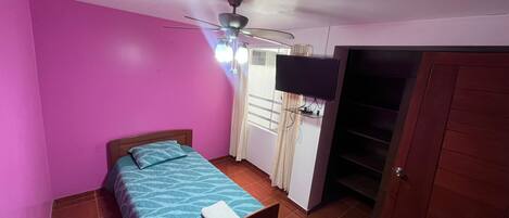 A bedroom with a bed, a ceiling fan, a TV, and a wardrobe.