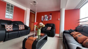 A living room with two black sofas, a glass coffee table, and a red accent wall.