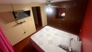 A bedroom with a bed, a TV mounted on the wall, a wardrobe, and a ceiling fan.