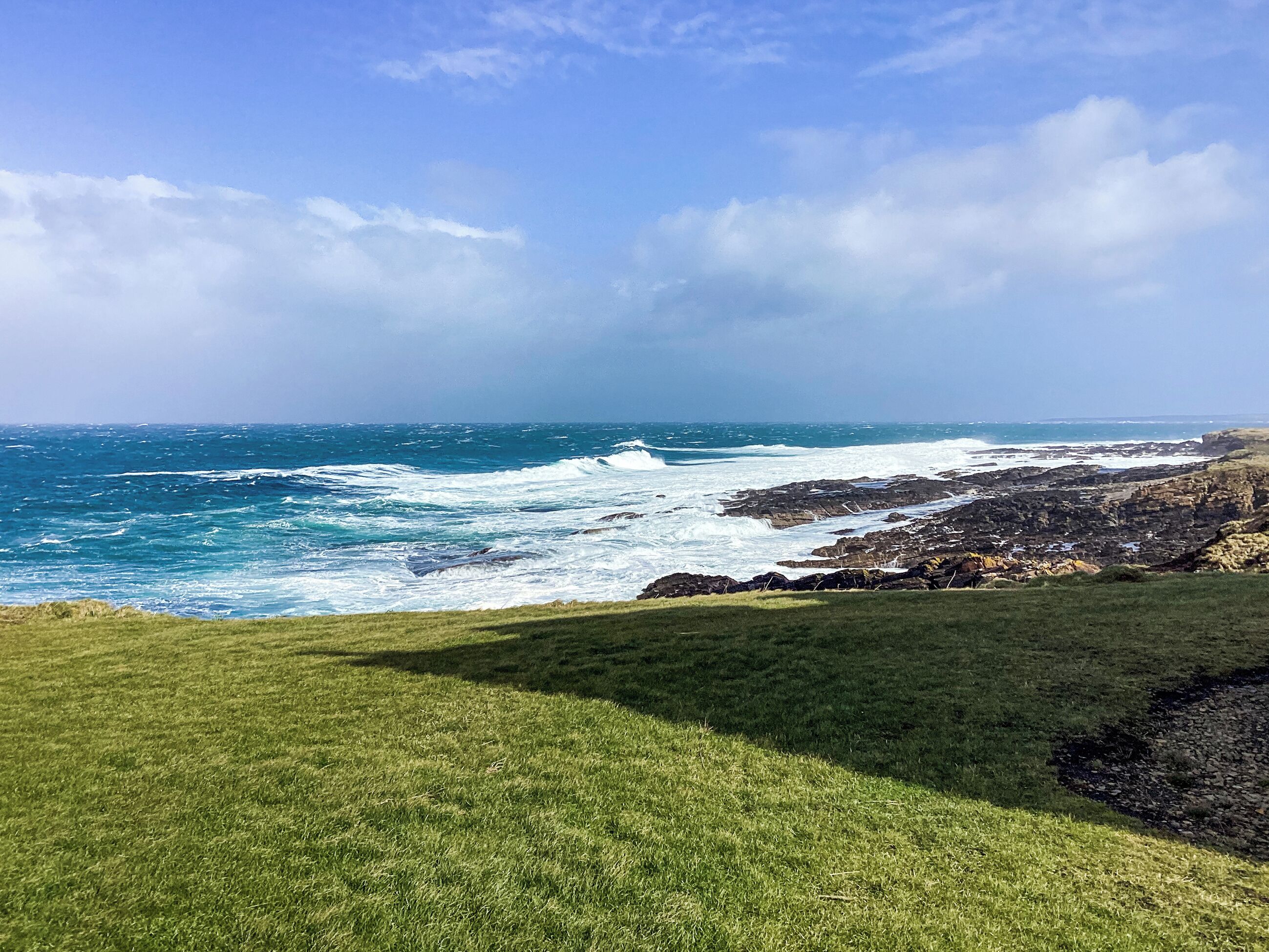 A coastal landscape with grassy terrain and rocky outcrops.