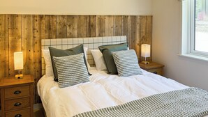 Una cama bien hecha con un edredón a rayas, dos mesitas de noche con lámparas y un cabecero de madera.