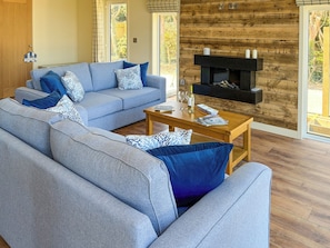 A modern living room with a grey sofa set, a wooden coffee table, and a fireplace. - 2 bedroom accommodation in Perranporth (Perranporth)