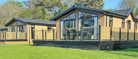 Une cabane en bois dotée d’une terrasse, de grandes fenêtres et d’une pelouse verdoyante.