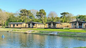 Una hilera de cabañas modernas de madera junto a un lago tranquilo, bajo un cielo despejado.