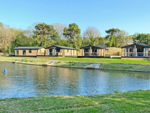 A row of modern, wooden cabins by a calm lake, with a clear sky above.