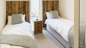 Un dormitorio con dos camas, un cabecero de madera, una mesita de noche con cajones y una ventana con persianas.