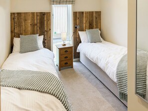A bedroom with two beds, a wooden headboard, a bedside table with drawers, and a window with blinds.