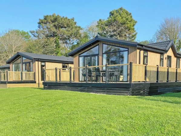 A wooden cabin with a deck, large windows, and a grassy lawn. - 2 bedroom accommodation in Perranporth (Perranporth)
