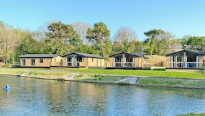 Une rangée de chalets modernes en bois, situés au bord d’un lac paisible, sous un ciel dégagé.