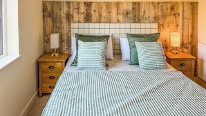 Un lit avec une couvre-lit à rayures, deux oreillers, une tête de lit en bois et deux tables de chevet avec des lampes.