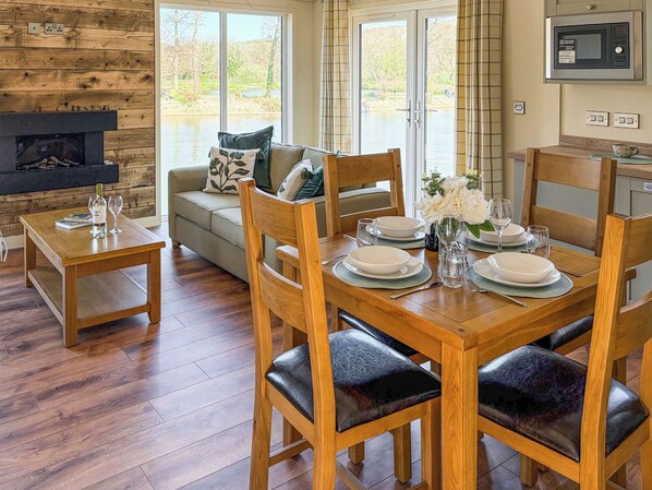 A dining area with a wooden table set for four, a sofa with cushions, and a fireplace.
