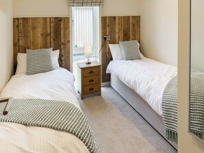 Een slaapkamer met twee bedden, houten hoofdborden, een nachtkastje met een lamp en uitzicht door een raam.