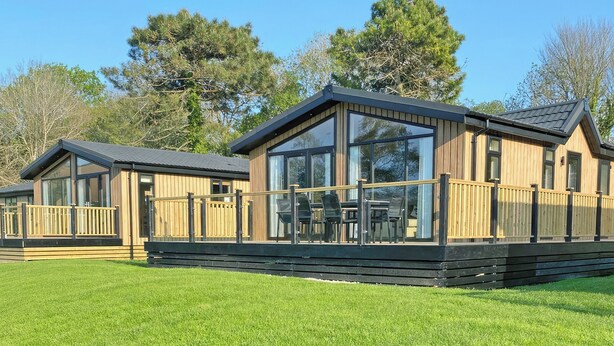 A wooden cabin with a deck, large windows, and a grassy lawn. - 3 bedroom accommodation in Perranporth (Perranporth)