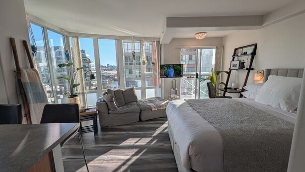 Moderni hotellihuone, jossa on suuri sänky, työpöytä, tuoli, televisio ja parveke, jolta on näkymä kaupunkiin.