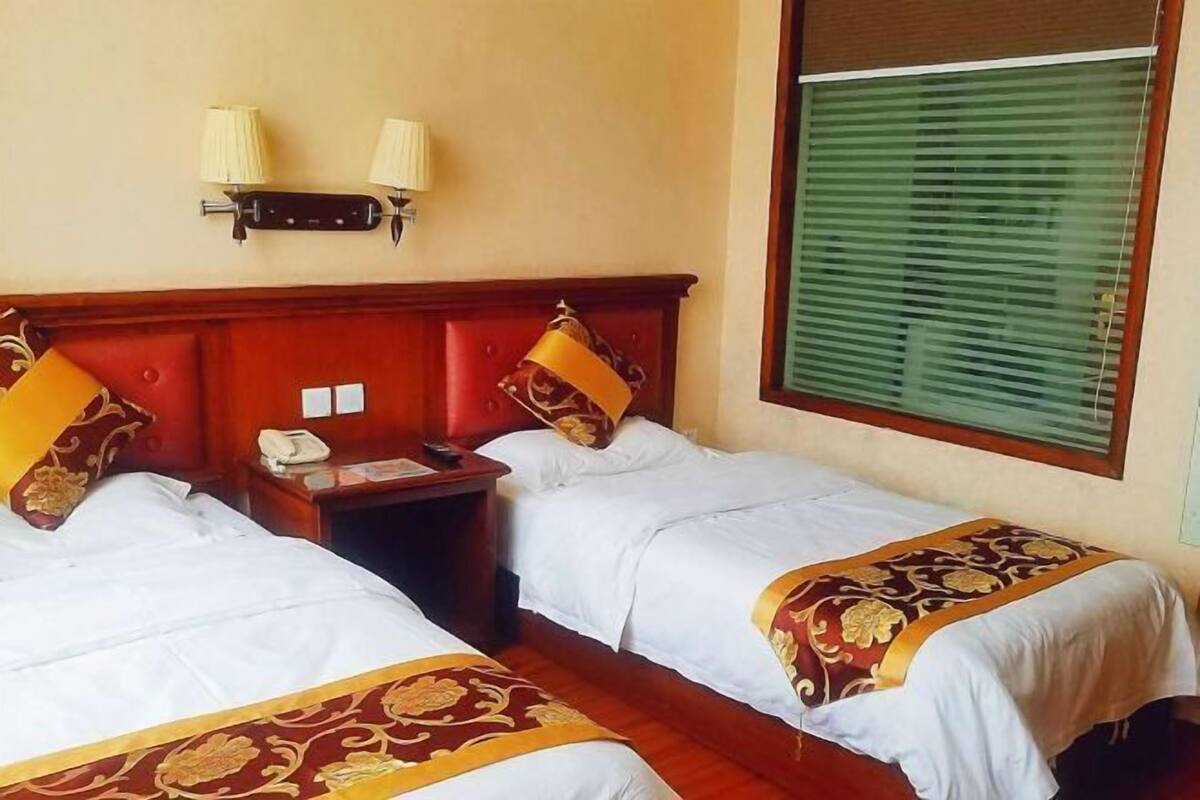 Habitació d'hotel amb dos llits, una taula de nit, un telèfon i una finestra amb persianes.