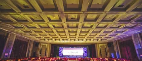 Une salle de conférence dotée d’une scène, de rangées de chaises et d’un plafond orné d’un motif en réseau.