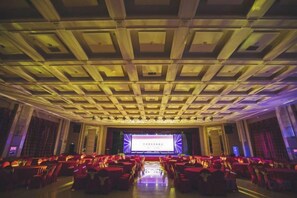 Un salón de conferencias con escenario, filas de sillas y un techo con diseño de cuadrícula.